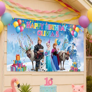 Op de afbeelding: Een groot spandoek met de tekst "HAPPY BIRTHDAY OLIVIA 5" toont personages uit de film Frozen. Kleurrijke ballonnen en slingers versieren de sc&egrave;ne. Een taart met het nummer 16 staat op de voorgrond.