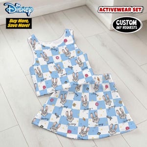 May include: A two-piece activewear set featuring a crop top and skirt. The set has a blue and white checkered pattern with cartoon rabbit faces, donuts, and other graphics. The Disney logo is visible.