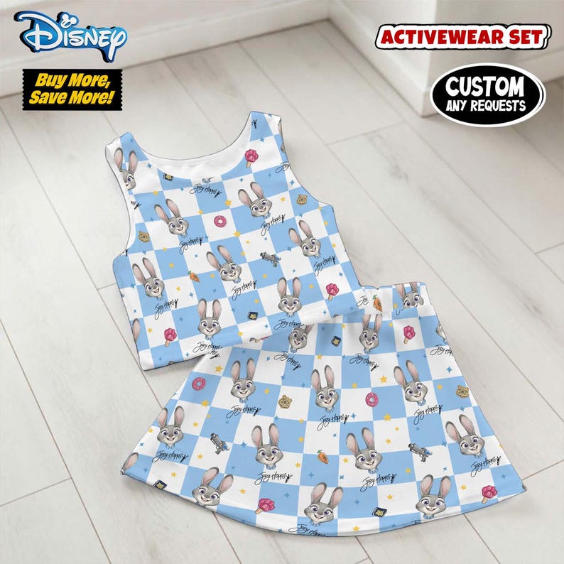 May include: A two-piece activewear set featuring a crop top and skirt. The set has a blue and white checkered pattern with cartoon rabbit faces, donuts, and other graphics. The Disney logo is visible.