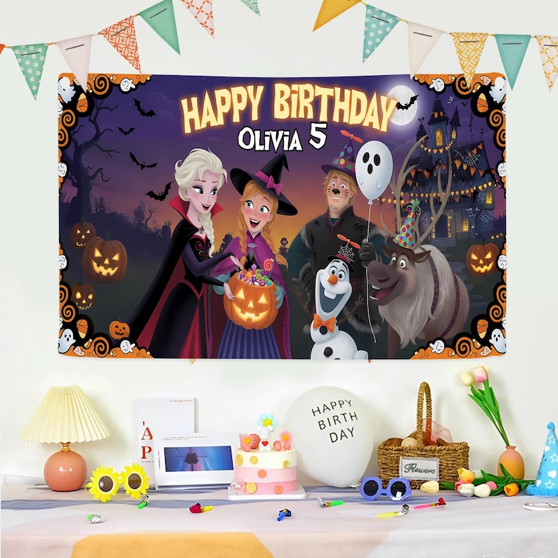 May include: A large birthday banner with the text "HAPPY BIRTHDAY OLIVIA 5" features characters from the movie Frozen in a Halloween-themed setting. The banner is decorated with pumpkins, bats, and a haunted house. Party decorations are in the foreground.