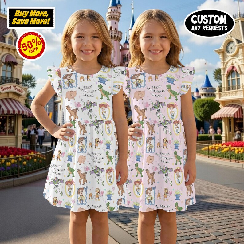 Puede incluir: Dos ni&ntilde;as peque&ntilde;as con vestidos blancos y rosas con estampado de Toy Story. Los vestidos tienen cuello redondo y mangas con volantes. El fondo muestra un parque tem&aacute;tico con tiendas y un castillo.