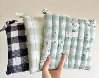 May include: Three quilted zippered pouches featuring fabric patterns. One pouch has a black and white gingham check, one has a light green and white gingham check, and the third has a light green gingham print with small white flowers and a label reading May Studio.