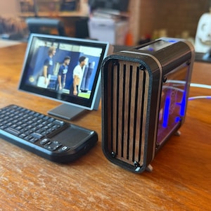 May include: A black computer keyboard with a touchpad and a small screen displaying a video. A black and wood-grain computer case with blue lights is next to the screen. The items are on a wooden surface.