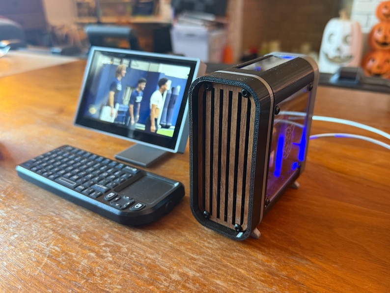 May include: A black computer keyboard with a touchpad and a small screen displaying a video. A black and wood-grain computer case with blue lights is next to the screen. The items are on a wooden surface.