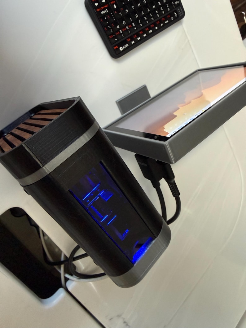 May include: A black and gray electronic device with a blue illuminated display, a tablet, and a small black keyboard. The device has a rectangular shape with a silver trim and a wooden top. The tablet is in a gray frame.