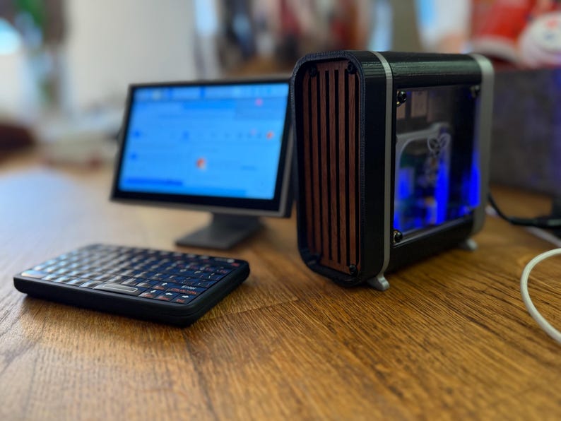 May include: A small computer setup featuring a black keyboard, a monitor displaying a blue screen, and a compact black and wood-toned computer case. The case has a clear side panel, revealing internal components.