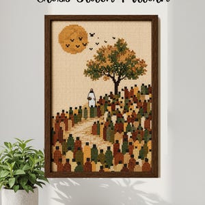 Puede incluir: Un patrón de punto de cruz enmarcado que muestra un paisaje con un árbol grande, un sol amarillo y una figura sobre una colina. La escena se compone de muchas formas pequeñas, coloridas y rectangulares en tonos marrón, verde y amarillo sobre tela beige.