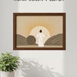 May include: A framed cross-stitch pattern depicting a religious scene with a figure in white robes standing before a rising sun. The text "Cross Stitch Pattern" is above the frame. The frame is brown.