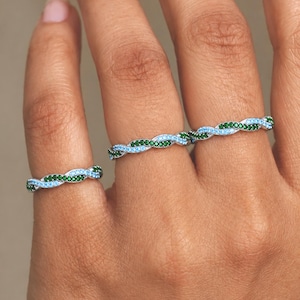 May include: Two silver-toned rings featuring a twisted design. Each ring is set with alternating rows of small, round, light blue and dark green stones that follow the spiral pattern of the metal band, creating a continuous, textured appearance.