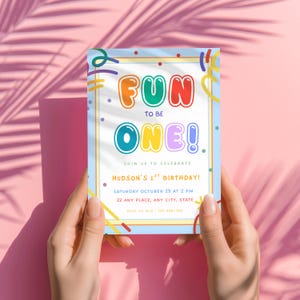 May include: A rectangular birthday invitation card with a light blue border and colorful confetti graphics. The text reads: FUN TO BE ONE! JOIN US TO CELEBRATE HUDSON'S 1ST BIRTHDAY! SATURDAY OCTOBER 29 AT 2 PM 22 ANY PLACE, ANY CITY, STATE RSVP TO MIA : 123-456-789