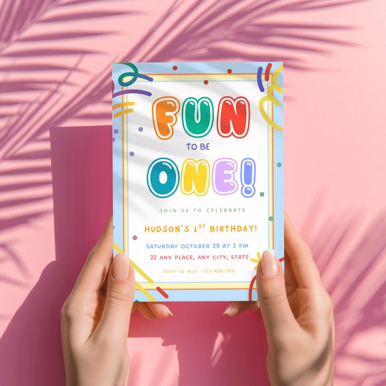 May include: A rectangular birthday invitation card with a light blue border and colorful confetti graphics. The text reads: FUN TO BE ONE! JOIN US TO CELEBRATE HUDSON'S 1ST BIRTHDAY! SATURDAY OCTOBER 29 AT 2 PM 22 ANY PLACE, ANY CITY, STATE RSVP TO MIA : 123-456-789
