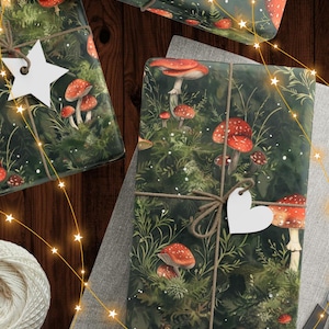 May include: Wrapped gifts with forest-themed wrapping paper featuring red and white mushrooms and green foliage. The gifts are tied with twine and adorned with white star and heart-shaped tags. Fairy lights and a ball of twine are also visible.