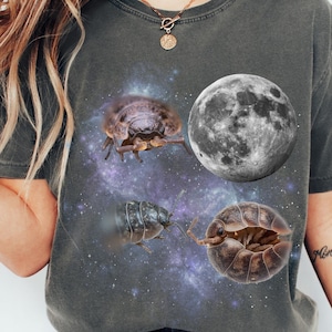 May include: Dark gray t-shirt featuring a graphic design of a full moon, three pill bugs, and a starry galaxy background. The pill bugs are in various positions, with one open. The shirt is a casual style.