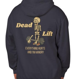 Puede incluir: Sudadera con capucha azul marino con un gráfico de un esqueleto levantando pesas. El texto "Dead Lift" está encima del esqueleto, y "Everything Hurts and I'm Hangry" debajo. La sudadera tiene una capucha con cordón.