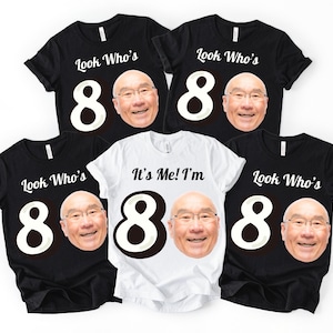 May include: A collection of black and white t-shirts with a large number 80 and a smiling face printed on them. One white t-shirt also features the same face and number 80, with the text "It's Me! I'm".