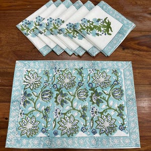 Puede incluir: Un juego de servilletas de algodón blancas y un mantel individual con un diseño floral. Las servilletas tienen un estampado floral azul y verde y un borde azul. El mantel individual tiene un fondo azul con un estampado floral blanco y un borde azul.