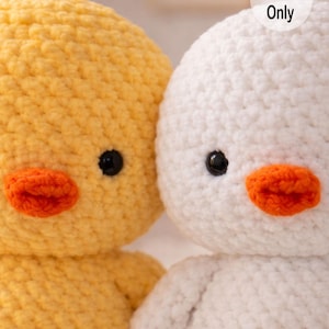 May include: Close-up of two crocheted duck toys. One is yellow, the other is white. Both have orange beaks and black eyes. The text "Pattern Only" is visible on the white duck. The toys are made of a soft, textured yarn.