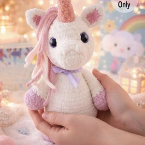 K&ouml;nnte beinhalten: Ein handgefertigtes wei&szlig;es H&auml;kel-Einhorn mit rosa Akzenten, einschlie&szlig;lich Horn, M&auml;hne und Hufen. Das Einhorn hat gro&szlig;e, dunkle Augen und ein lila Band um den Hals. Der Text "Pattern Only" ist enthalten.