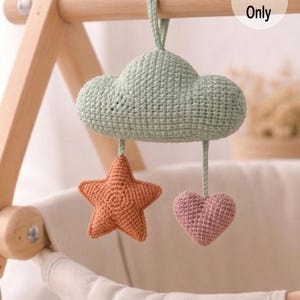 May include: A handmade crochet baby mobile featuring a mint green cloud, an orange star, and a pink heart. The mobile is suspended from a wooden frame. The text "Pattern Only" is visible.