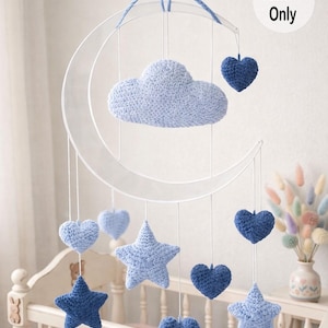 May include: A baby mobile featuring a crescent moon frame with hanging crochet shapes. The mobile includes a light blue cloud, stars, and hearts in varying shades of blue. The text "Pattern Only" is visible.