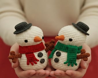Può includere: Due piccole statuette di pupazzi di neve all'uncinetto, ciascuna con un cappello grigio scuro, un naso arancione a forma di carota e braccia marroni simili a ramoscelli. Un pupazzo indossa una sciarpa rossa, l'altro verde. Testo: pattern Only.