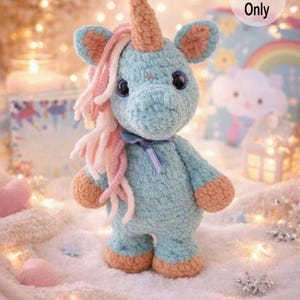 K&ouml;nnte beinhalten: Geh&auml;keltes Einhorn-Spielzeug in Hellblau, mit einer pfirsichfarbenen Horn, Hufen und Ohrenakzenten. Das Einhorn hat rosa und wei&szlig;e Garnhaare, gro&szlig;e dunkle Augen und ein blaues Band. Das Bild hat eine weiche, vertr&auml;umte &Auml;sthetik, mit einem "Pattern Only"-Aufkleber.