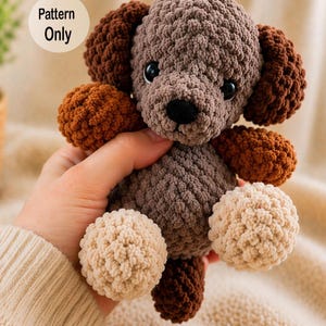 Puede incluir: Peluche de perro de ganchillo hecho a mano en tonos marrones y beige. El perro tiene orejas, patas y cola de color marrón oscuro, cuerpo marrón claro y patas beige. El texto "Pattern Only" está en un círculo blanco.