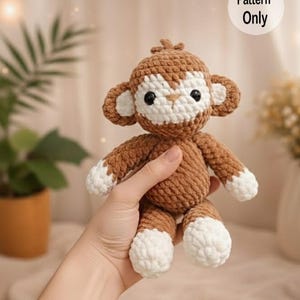 May include: Crocheted monkey plush toy in brown and white. The monkey has a white face, ears, and feet, with black eyes. The text "Pattern Only" is in a white circle in the upper right corner.