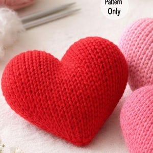 Peut inclure: Un cœur rouge tricoté à la main, avec une surface texturée et une forme arrondie. L'image montre également des pelotes de laine roses, des aiguilles à tricoter et un cœur rose tricoté. Le texte "Pattern Only" est visible.