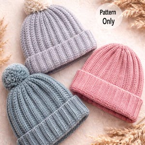 May include: Three knitted beanies in shades of gray, blue, and pink. The gray beanie has a cream-colored pom-pom, while the blue beanie has a blue pom-pom. The pink beanie is without a pom-pom. The text "Pattern Only" is visible.
