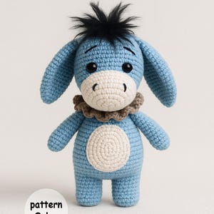 May include: A handmade blue crochet donkey with a white belly and muzzle, black eyes, and a brown ruffled collar. The donkey has black fuzzy hair on top of its head. The text "pattern Only" is in a white circle.