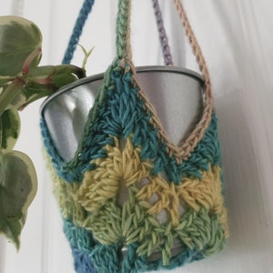 Puede incluir: Un macetero de crochet con una maceta plateada, con un diseño multicolor de hilo azul, verde y amarillo.