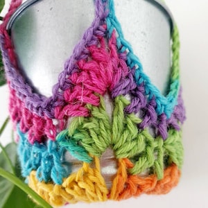 May include: A colourful crocheted plant hanger with a silver metal pot. The hanger is made with a rainbow of colours, including purple, pink, green, blue, yellow, and orange.