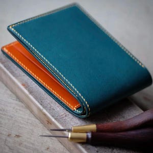 Cartera plegable italiana de curtido vegetal, hecha a mano. Exterior azul medianoche con forro naranja ámbar y bordes bruñidos.
