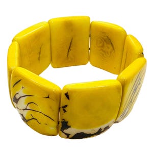 May include: A yellow bracelet with rectangular, curved segments. The bracelet has a glossy finish and features dark brown and white accents on some segments. The bracelet is designed to be worn around the wrist.