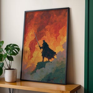 Könnte beinhalten: Gerahmter Kunstdruck mit einer Silhouette, die ein Schwert hält, vor einem feurigen, orange-roten Himmel. Die Figur ist in einen Umhang gehüllt und steht auf einer grünen und grauen Landschaft. Das Kunstwerk ist in einem schwarzen Rahmen ausgestellt.