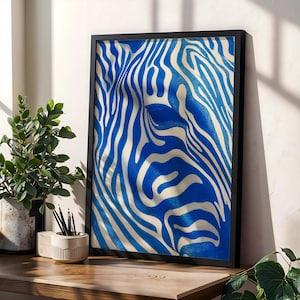 Op de afbeelding: Een ingelijste kunstprint met een blauw en wit zebra streepjespatroon. Het kunstwerk is in een zwarte lijst en staat op een houten oppervlak. De print is een modern decoratief stuk.