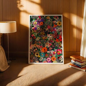K&ouml;nnte beinhalten: Ein gerahmter Kunstdruck mit einem lebendigen Blumenmuster, das farbenfrohe Blumen in Rot-, Orange-, Gelb-, Rosa- und Lilat&ouml;nen zeigt. Das Kunstwerk steht auf einem braunen Boden, gelehnt an einer Holzwand. Ein Stapel B&uuml;cher und eine Lampe sind ebenfalls zu sehen.
