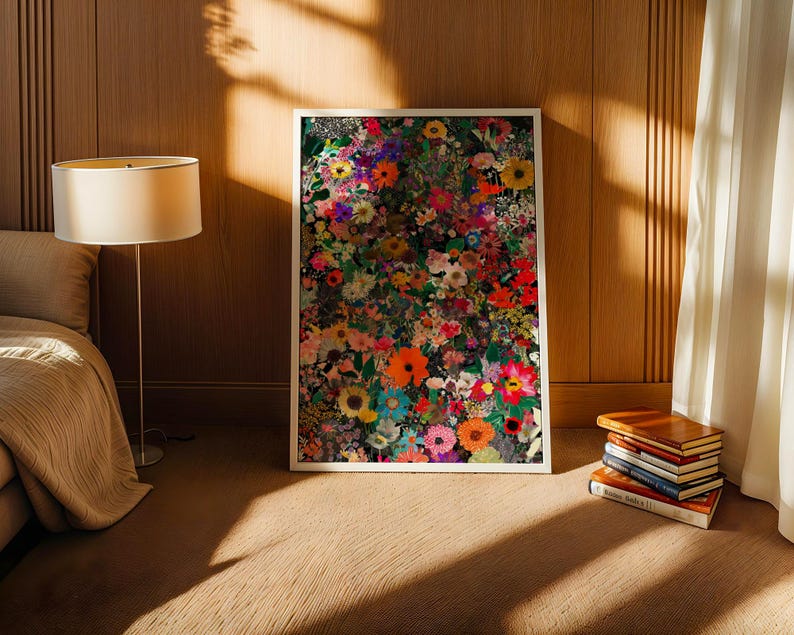 K&ouml;nnte beinhalten: Ein gerahmter Kunstdruck mit einem lebendigen Blumenmuster, das farbenfrohe Blumen in Rot-, Orange-, Gelb-, Rosa- und Lilat&ouml;nen zeigt. Das Kunstwerk steht auf einem braunen Boden, gelehnt an einer Holzwand. Ein Stapel B&uuml;cher und eine Lampe sind ebenfalls zu sehen.