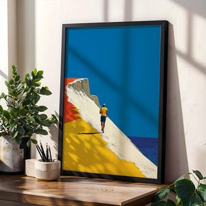 May include: A framed art print featuring a minimalist illustration of a person in a yellow shirt and blue shorts walking along a white cliff edge. The composition includes bold blocks of deep blue, bright yellow, and red against the white cliff.