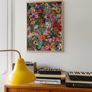 K&ouml;nnte beinhalten: Ein gerahmter Kunstdruck mit bunten Blumen in Rot-, Orange-, Gelb-, Blau- und Lilat&ouml;nen. Das Kunstwerk h&auml;ngt an einer wei&szlig;en Wand &uuml;ber einem Holzschrank mit einer gelben Lampe und Musikequipment.