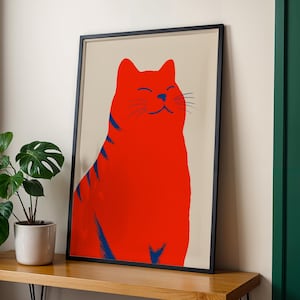 Könnte beinhalten: Ein gerahmter Kunstdruck mit einer stilisierten Illustration einer leuchtend roten Katze mit dunkelblauen Streifen auf hellbeigem Hintergrund. Die Katze ist in sitzender Position dargestellt, mit geschlossenen Augen und einem leichten Lächeln.