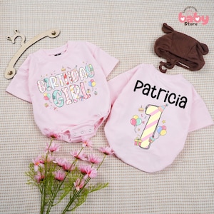 May include: Pink baby bodysuit with the text "BIRTHDAY GIRL" in colorful letters and graphics. A matching pink t-shirt with the name "Patricia" and the number "1" with party graphics. A brown bear-eared hat is also included.