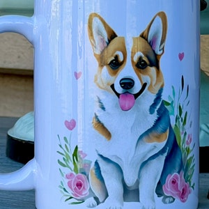 May include: White ceramic mug with a colorful illustration of a corgi dog sitting with pink flowers and hearts.