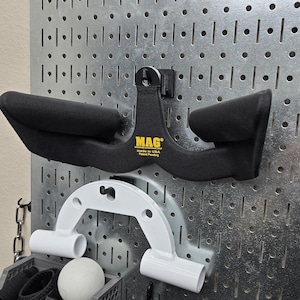 May include: A black MAG Maximum Advantage Grip weightlifting handle with padded grips is mounted on a metal pegboard. Below it is a white weightlifting handle. A gray storage bin holds various fitness accessories.