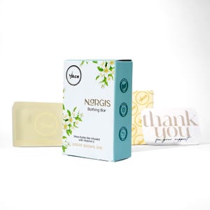 Könnte beinhalten: Eine Auswahl an Nargis Bathing Bar Produkten. Das Hauptprodukt ist eine weiße und türkisfarbene Schachtel mit dem Markennamen und floralem Design. Ein Seifenstück und eine Dankeskarte sind ebenfalls zu sehen.