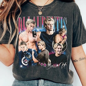 Pode incluir: T-shirt cinza escuro com uma colagem de imagens de um homem com cabelo loiro. A camisa tem o texto "LAURENTIS" em uma fonte retr&ocirc;, com o nome "Briar U" abaixo. O design inclui estrelas e uma imagem com tema de h&oacute;quei.