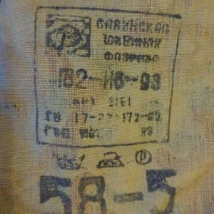 May include: A tan fabric surface featuring a black ink stamp with Cyrillic text, including the characters ПВ2-ИВ-93, 17-2, 172-62, and 93. Below the stamp are laundry care symbols and the large black printed numbers 58-5 on the textured material.
