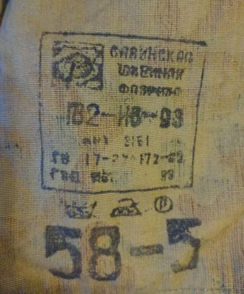May include: A tan fabric surface featuring a black ink stamp with Cyrillic text, including the characters ПВ2-ИВ-93, 17-2, 172-62, and 93. Below the stamp are laundry care symbols and the large black printed numbers 58-5 on the textured material.