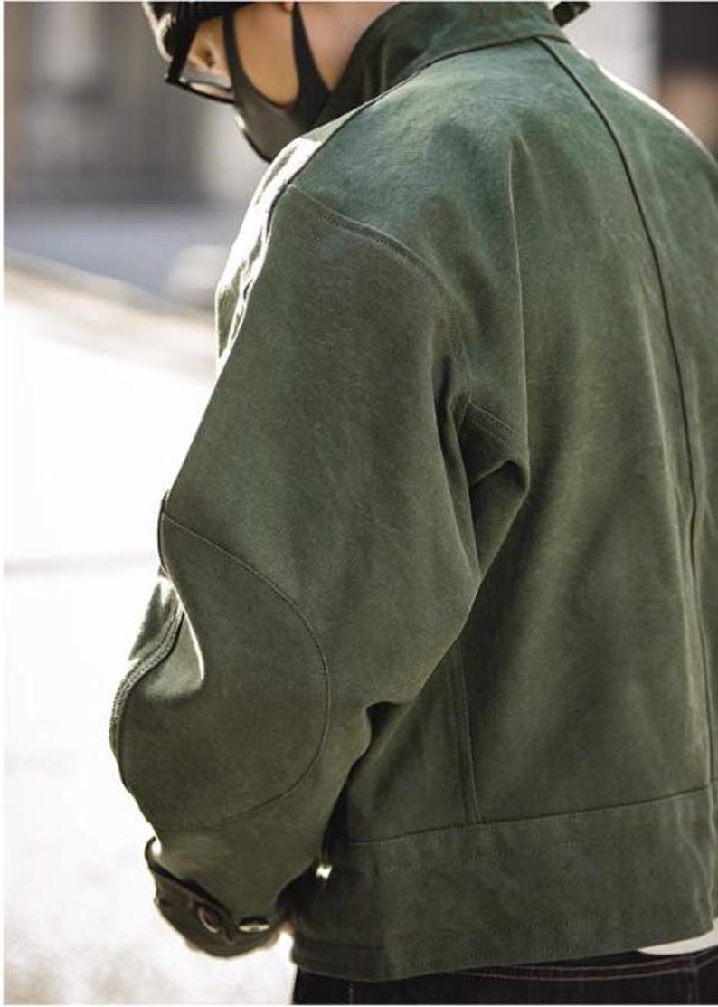 May include: A green jacket with a textured appearance. The jacket features a classic design with a button closure and a structured fit. The sleeves have a curved design at the elbows. The jacket is made of a durable material.